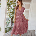 Woman wearing a red floral dress standing on a wooden deck with greenery in the background