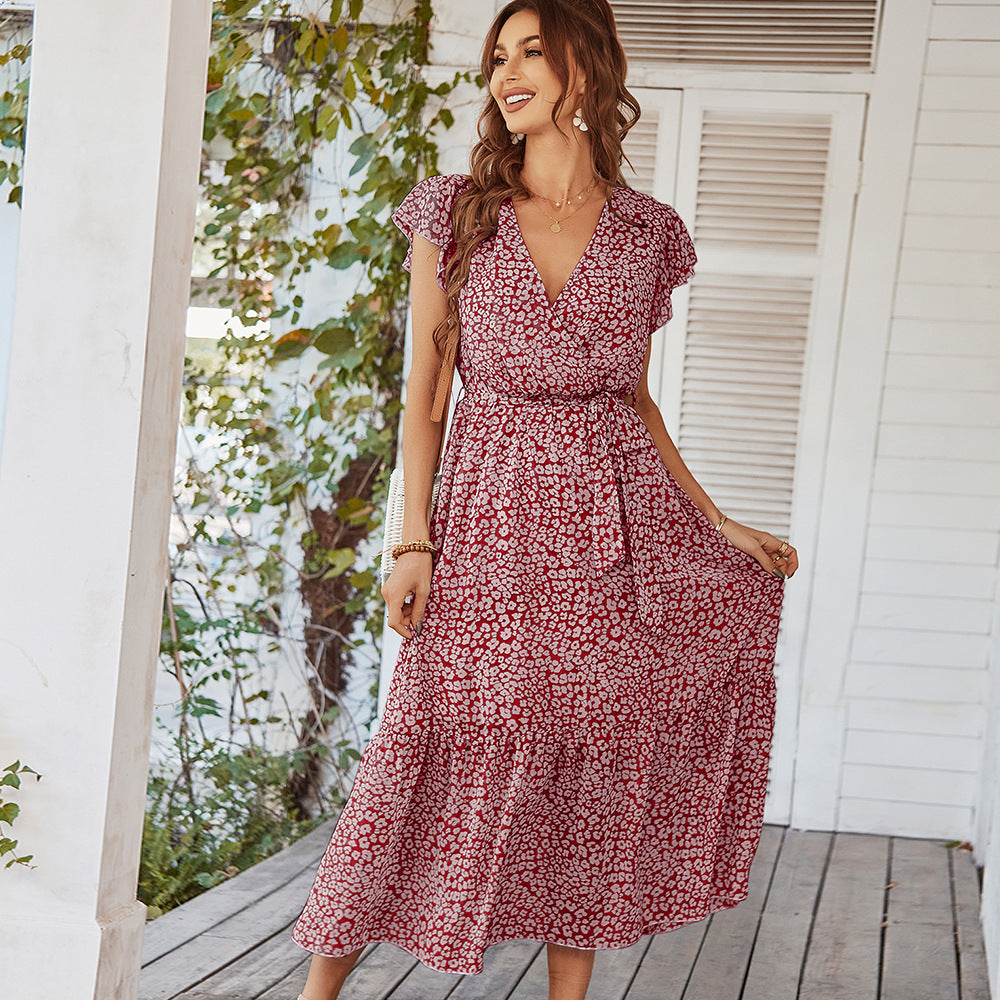 Woman wearing a red floral dress standing on a wooden deck with greenery in the background