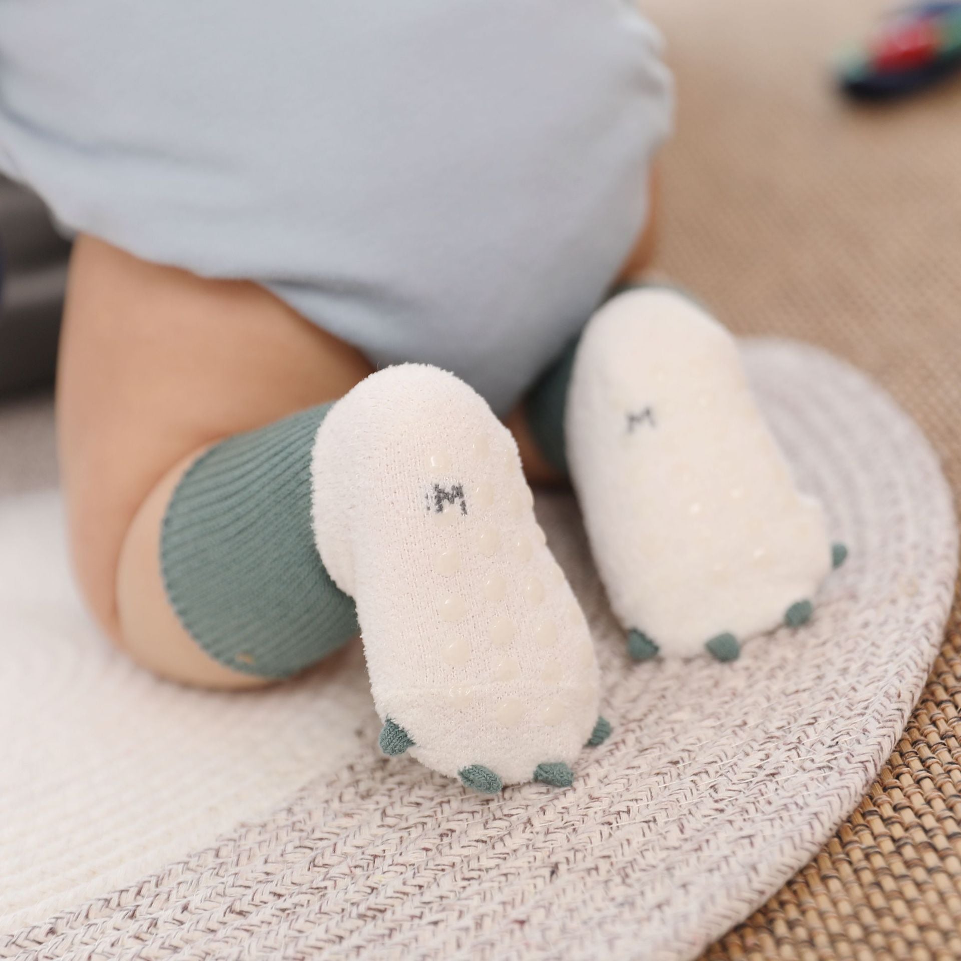 Baby's feet wearing white socks with green accents on a textured surface