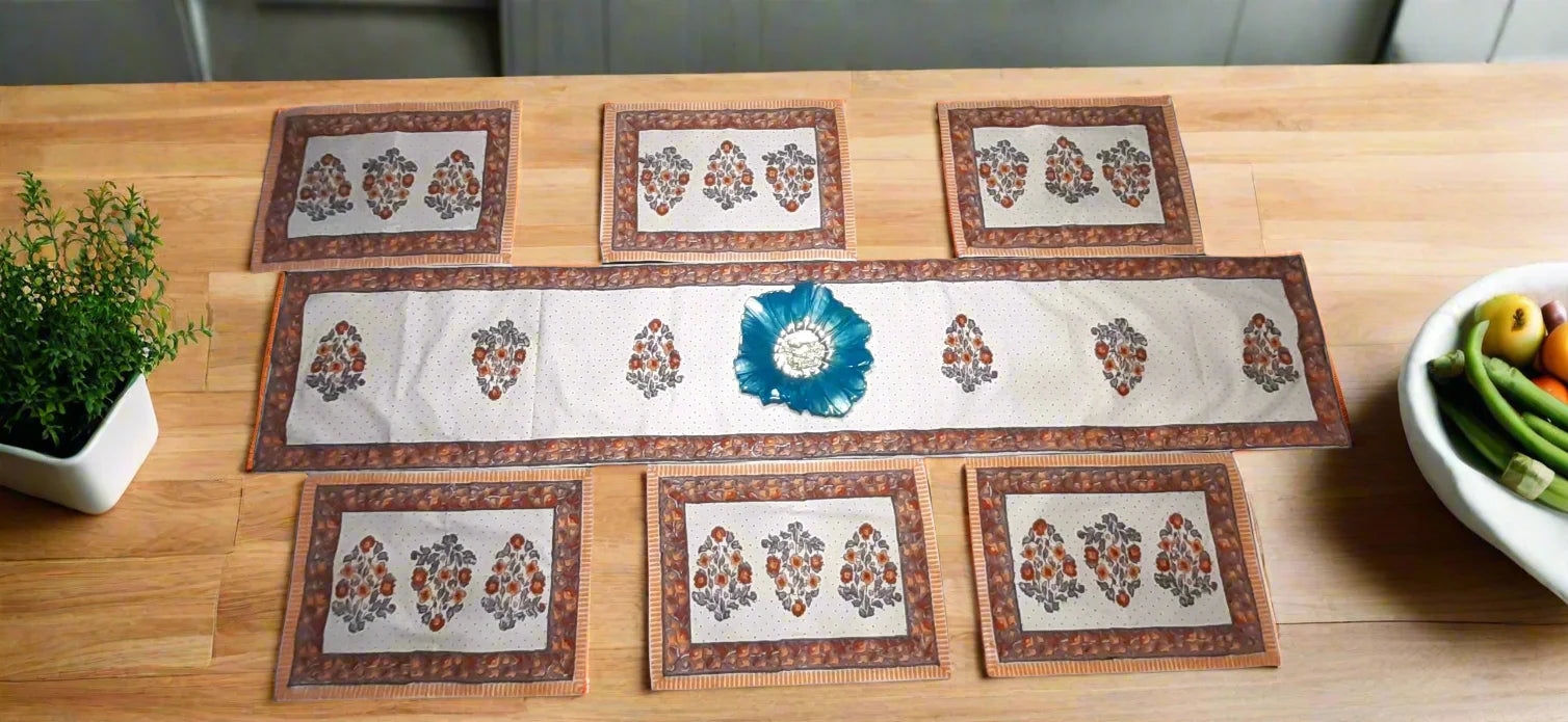 Set of decorative placemats on a wooden table with a plant and bowl in the background.