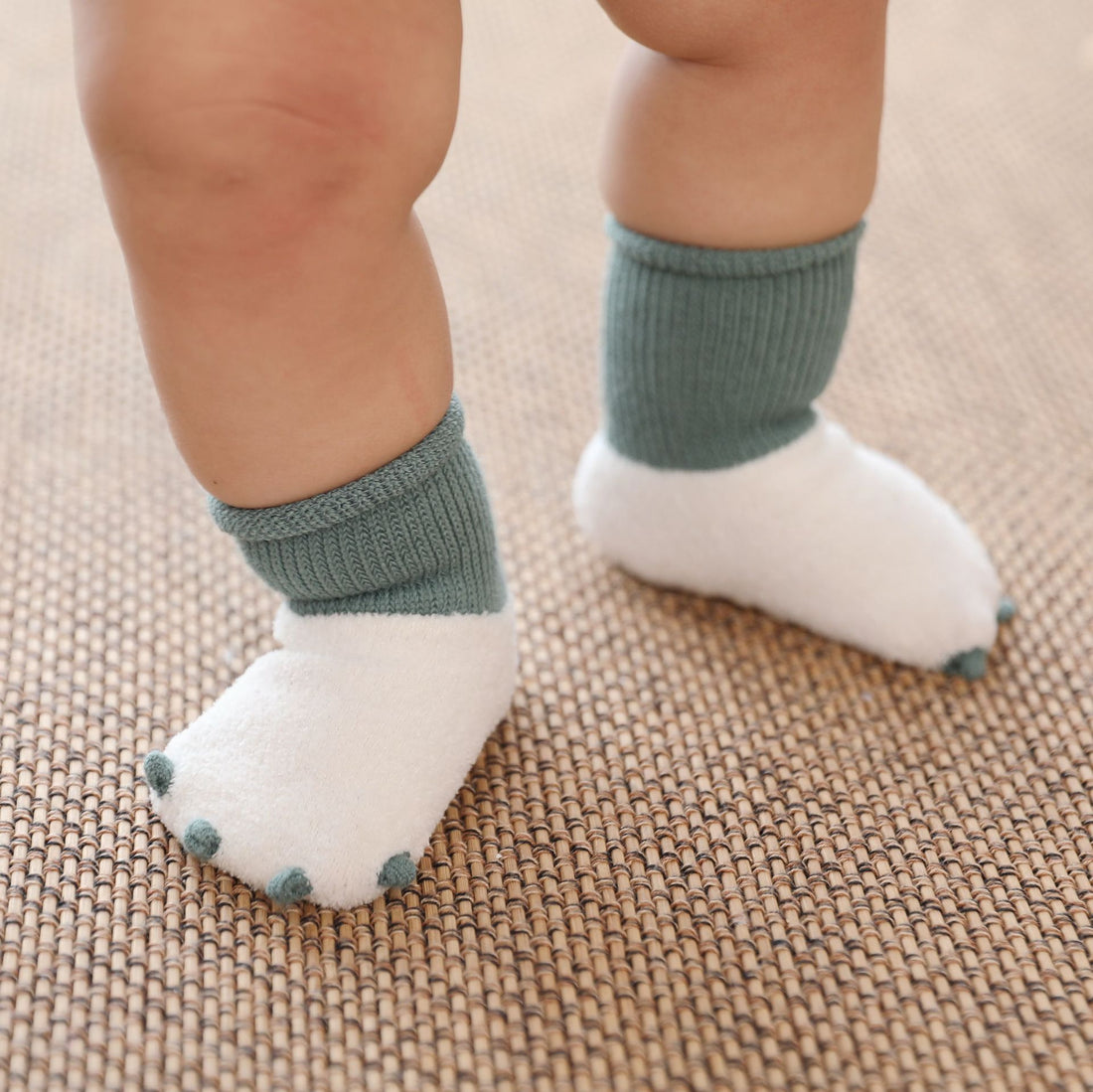 Baby feet wearing white socks with green cuffs on a textured surface
