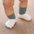 Baby feet wearing white socks with green cuffs on a textured surface