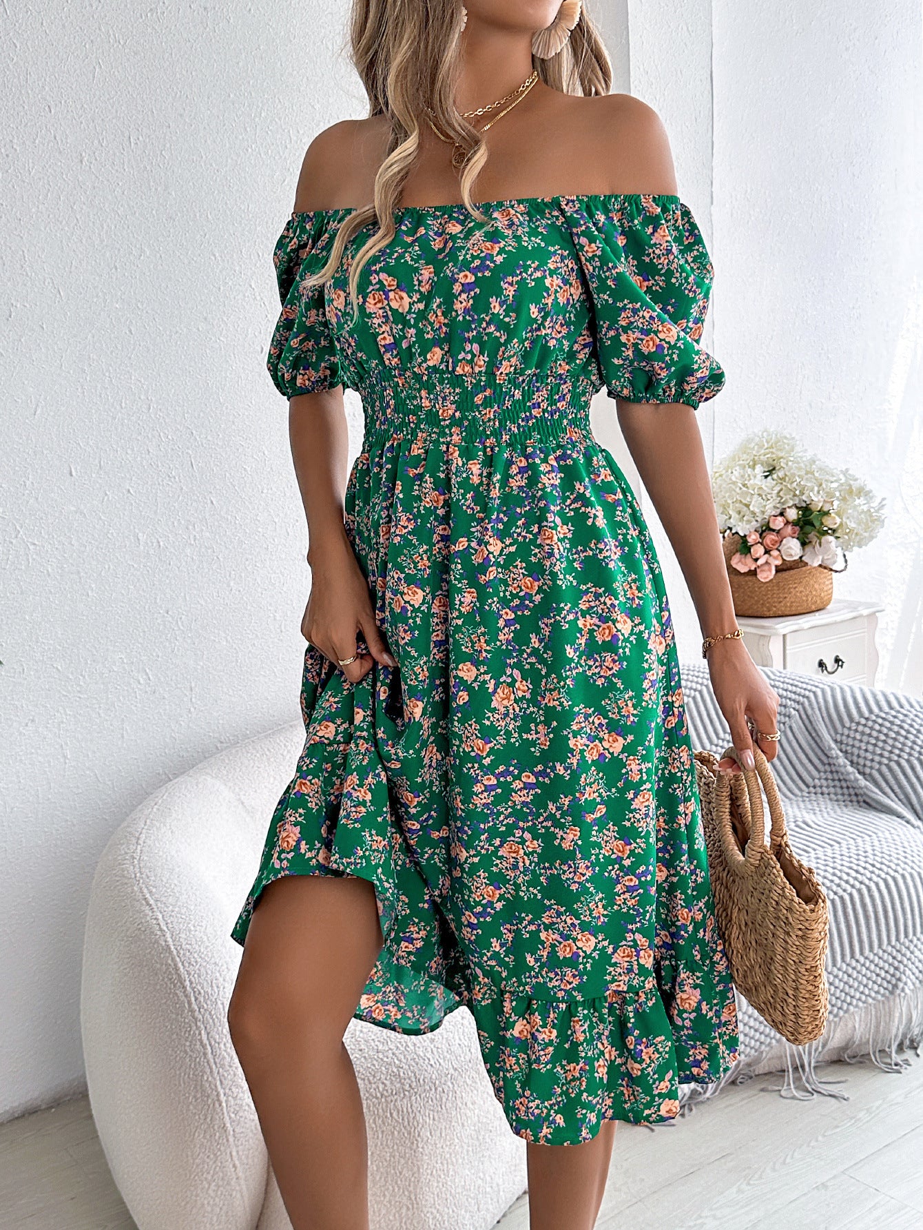 Woman wearing a green floral off-shoulder dress in a bright room.