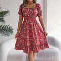 Woman wearing a red floral dress sitting on a white chair with a plant in the background